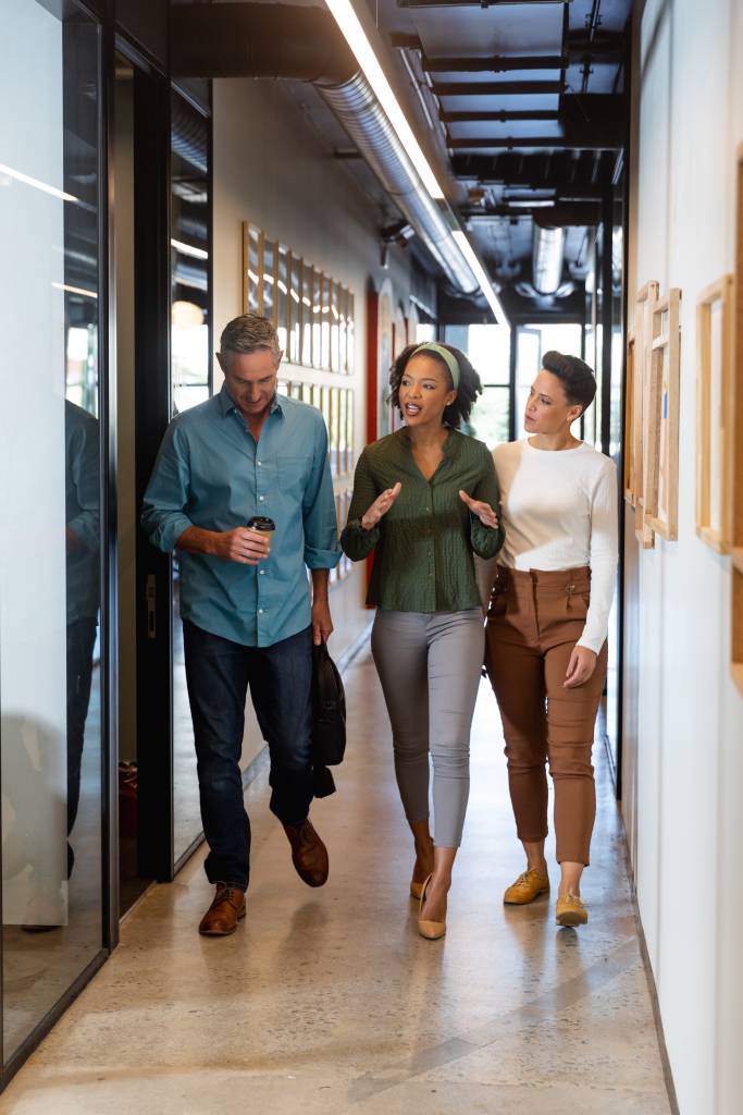 Multiracial businessman and businesswomen discussing while walking in corridor of office building